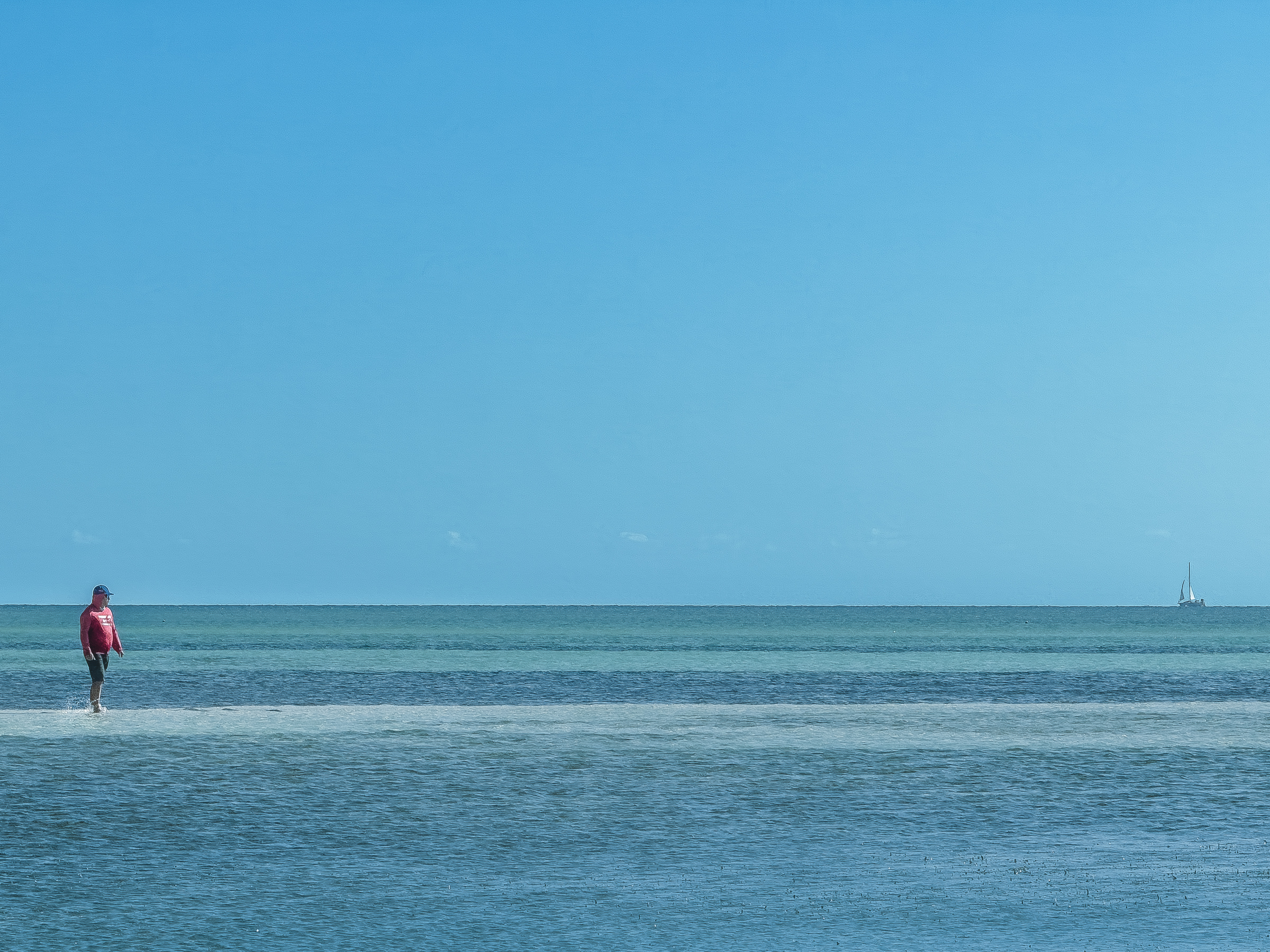 Figura humana caminhando no mar sob céu azu.